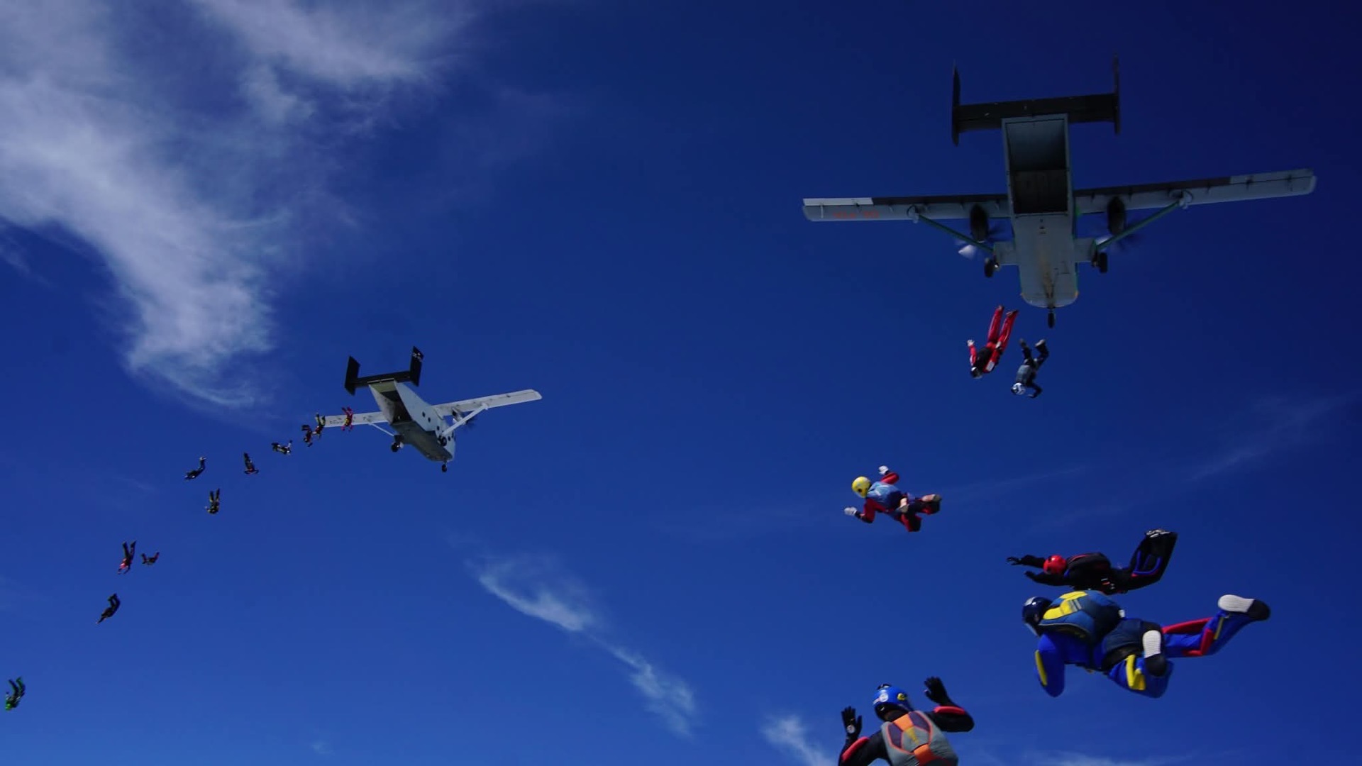Dos aviones soltando paracaidistas en cadena sobre un cielo despejado