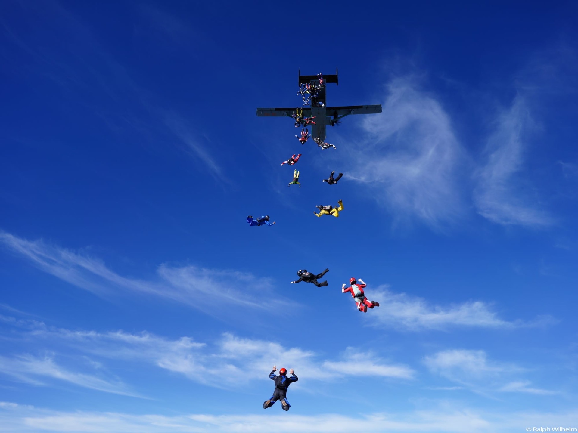 Paracaidistas saliendo en cadena de un avión sobre un cielo azul